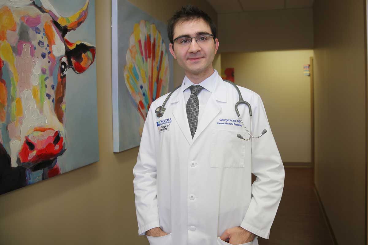 Doctor wearing glasses, white coat and stethoscope stands in hallway