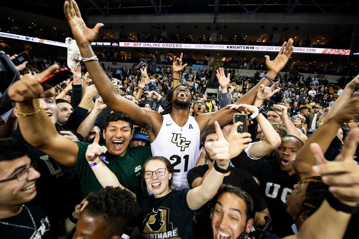 men's basketball player Chad Brown lifts arms in the air to celebrate with fans surrounding him