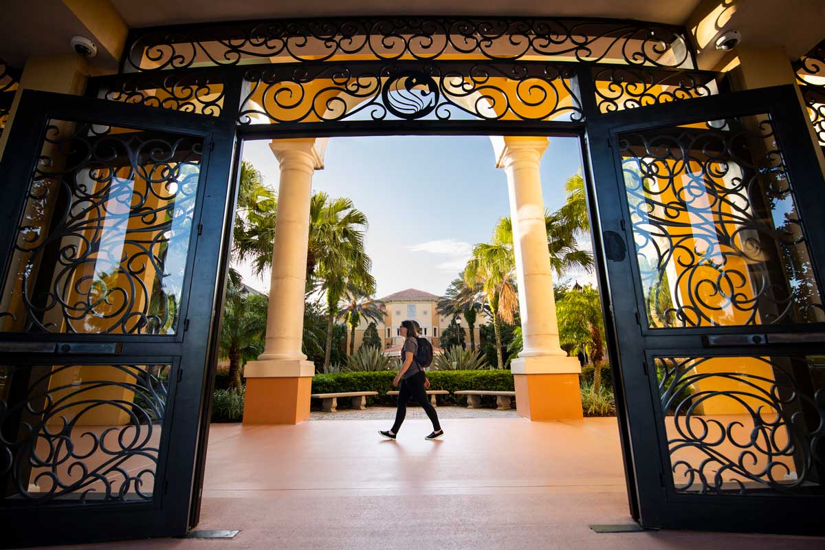 Female student wearing a backpack walks across courtyard entrance