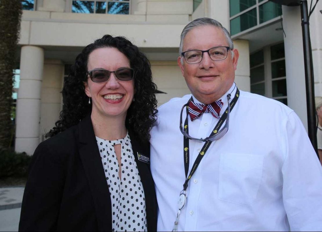 Man wearing white shirt with bow tie stands next to woman wearing black sweater