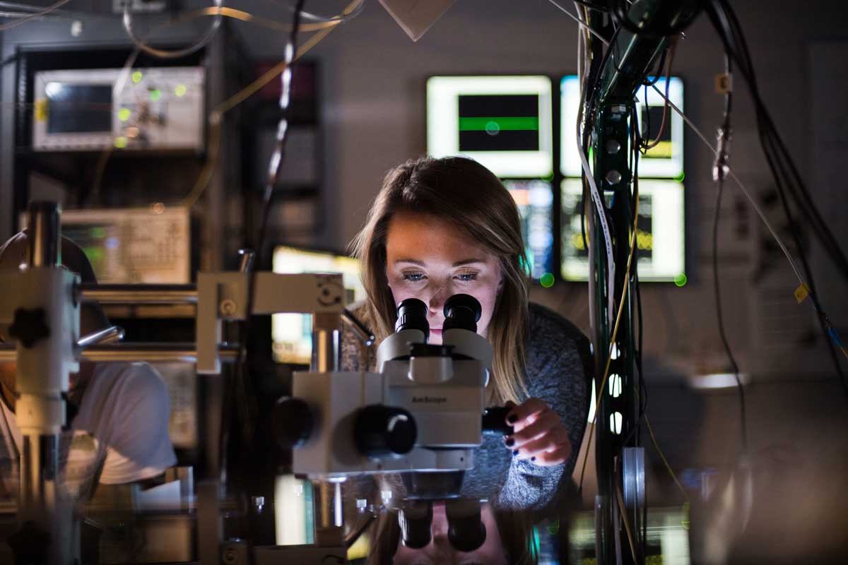 Blonde woman looks into a microscope in a lab