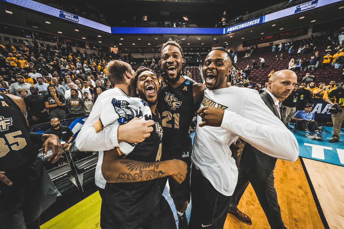 Three basketball players hug and celebrate on court