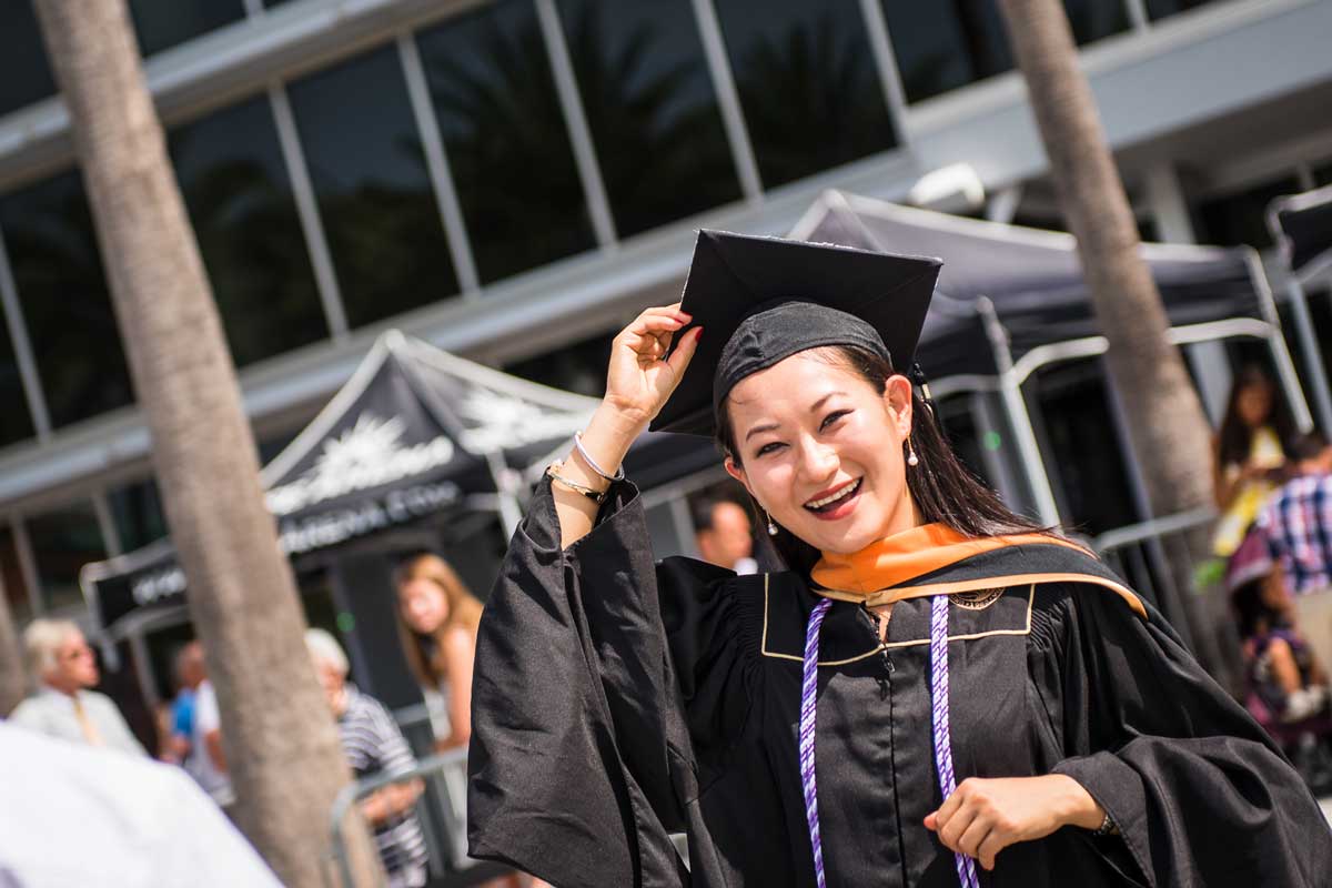 Woman in cap and gown smiles outside arena