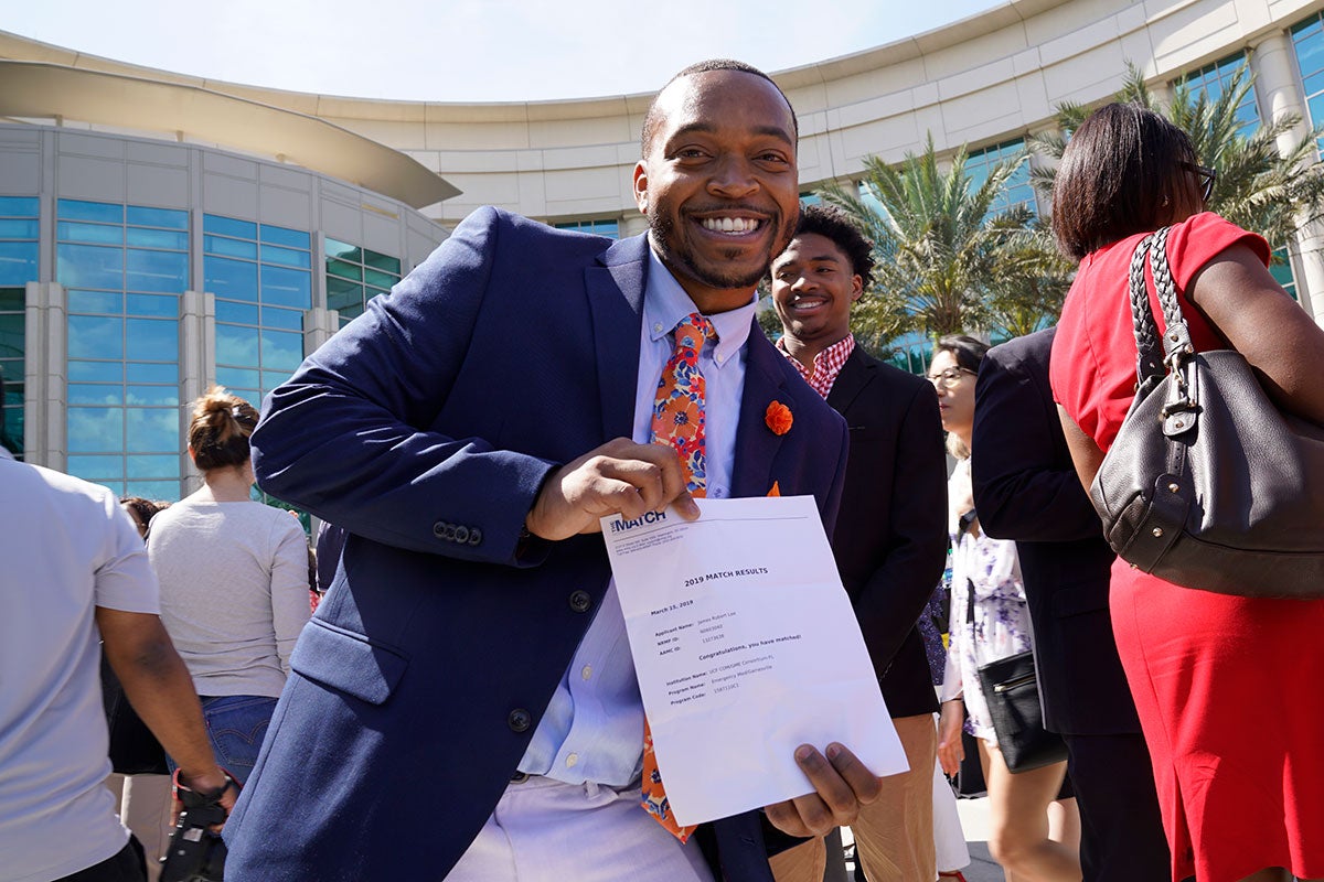 Man wearing a suit holds a piece of paper and smiles