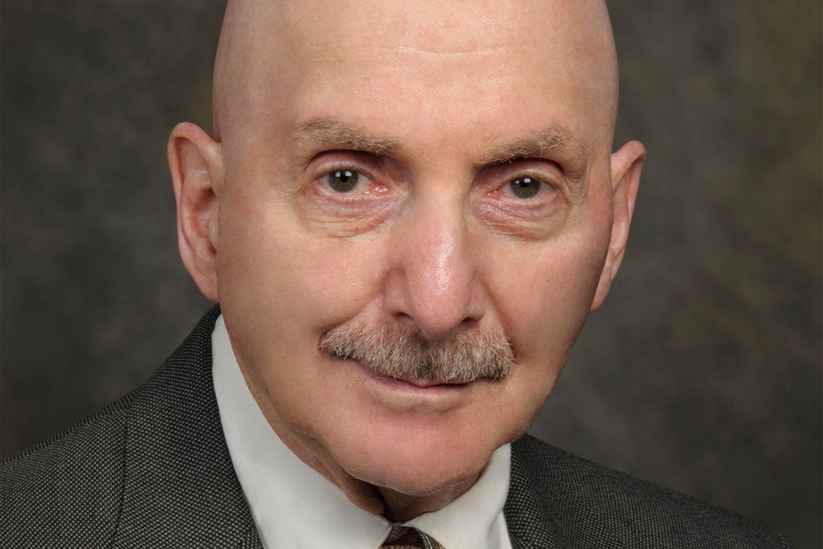 A close-up headshot of white man with a moustache