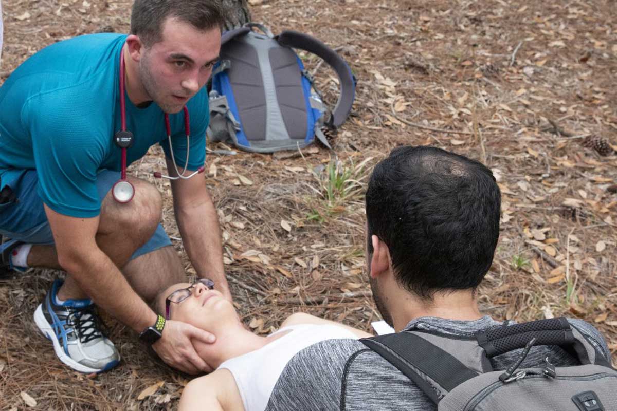 man kneels next to woman on the ground and holds her neck to take her pulse