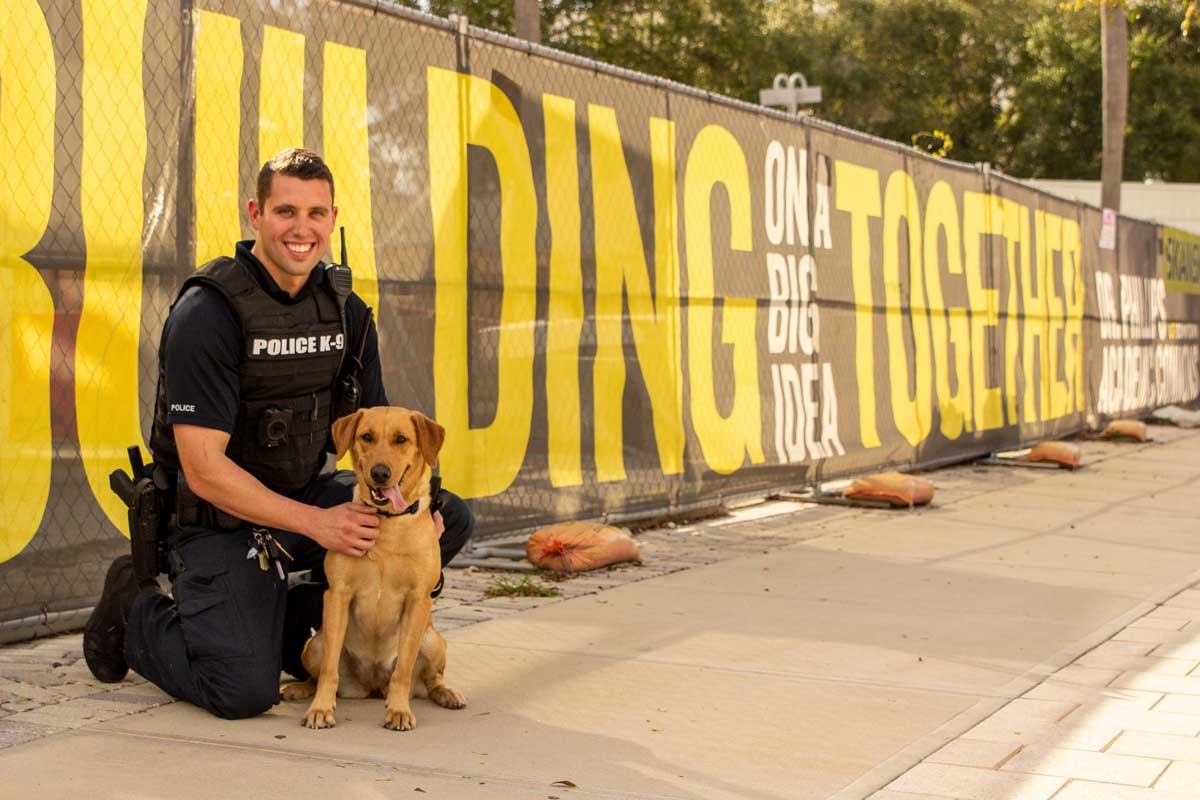 Police officer kneels next to golden lab on sidewalk