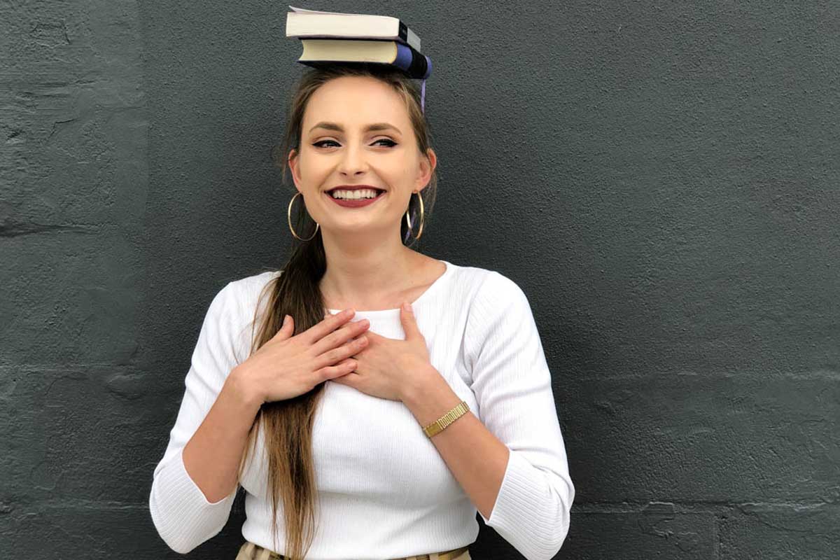 Young woman wearing white long sleeve shirt balances two books on her head