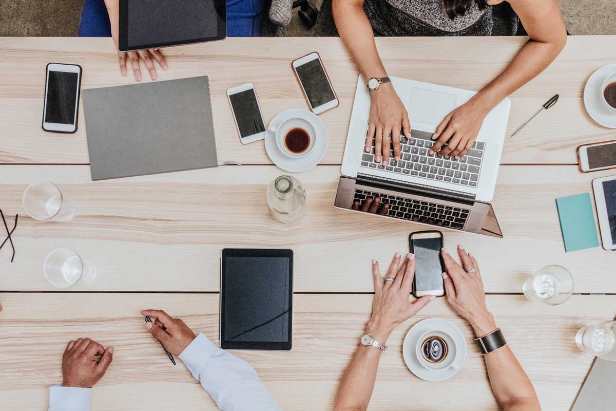 team of people sitting at table with laptops and tablets