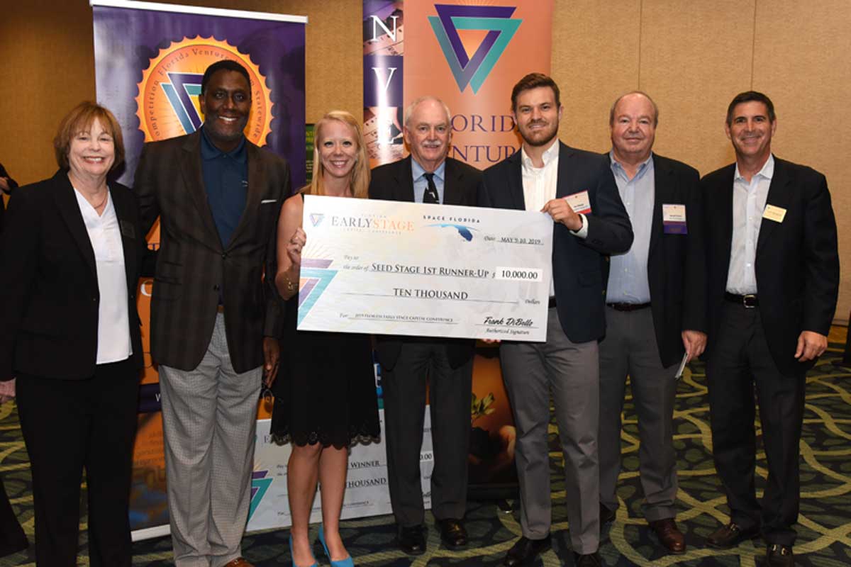 Group of seven people stand with a large check in ballroom