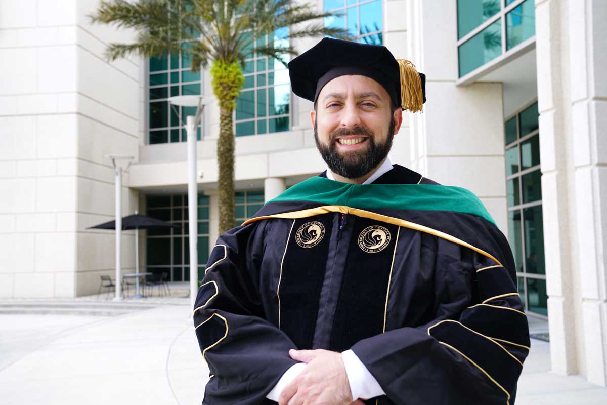 Graduate stands in front of white building and palm tree