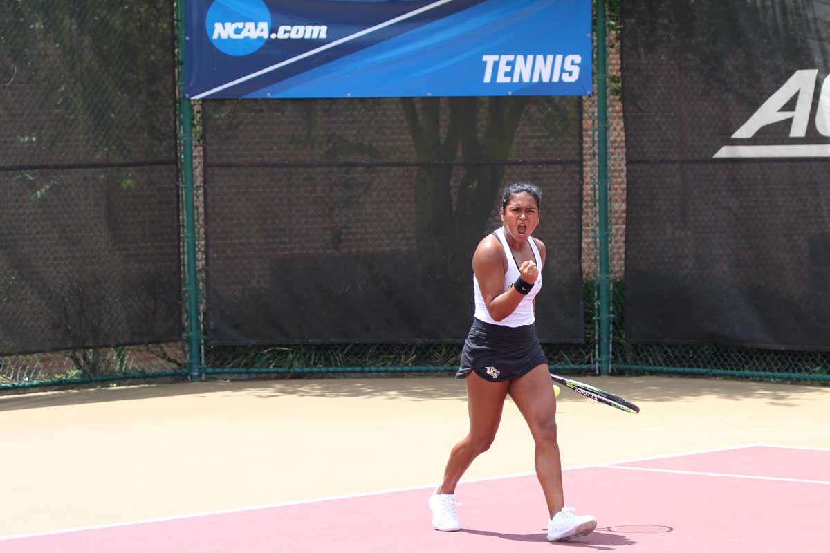 Female tennis player clenches fist in celebration on red and yellow court