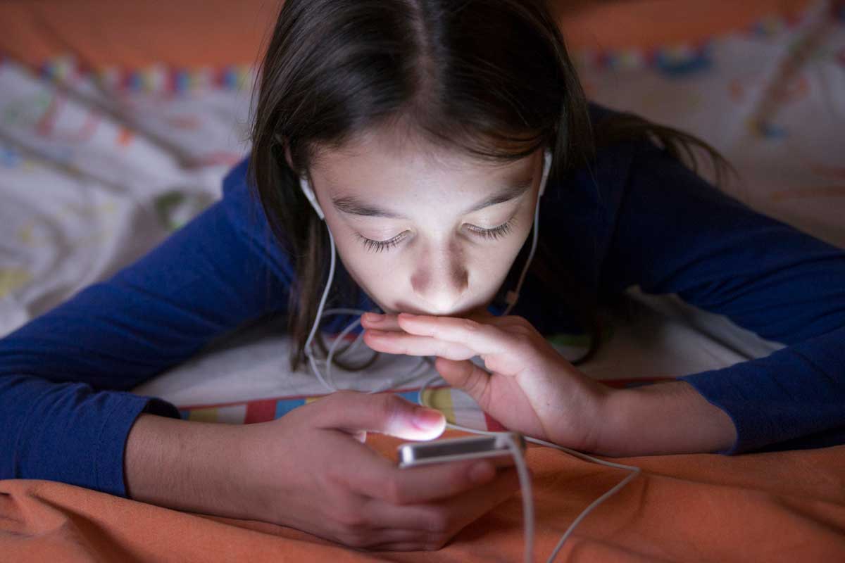 Young girl lays on her stomach looking at her cell phone screen