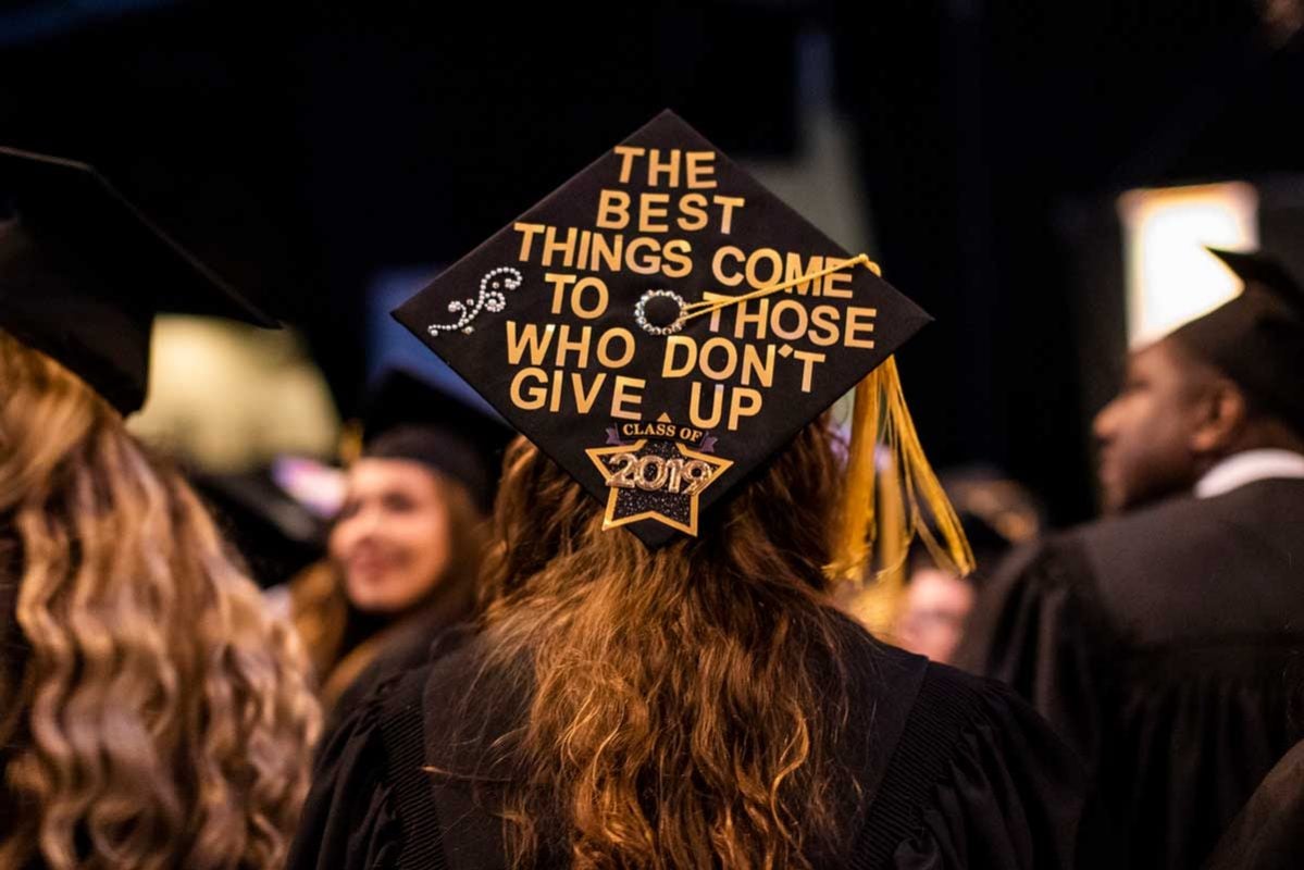 Female graduate wears cap that says "The Best Things Come to Those Who Don't Give Up"