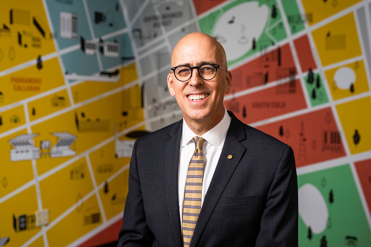 A man in black suit and yellow tie stands in front of a map of downtown Orlando