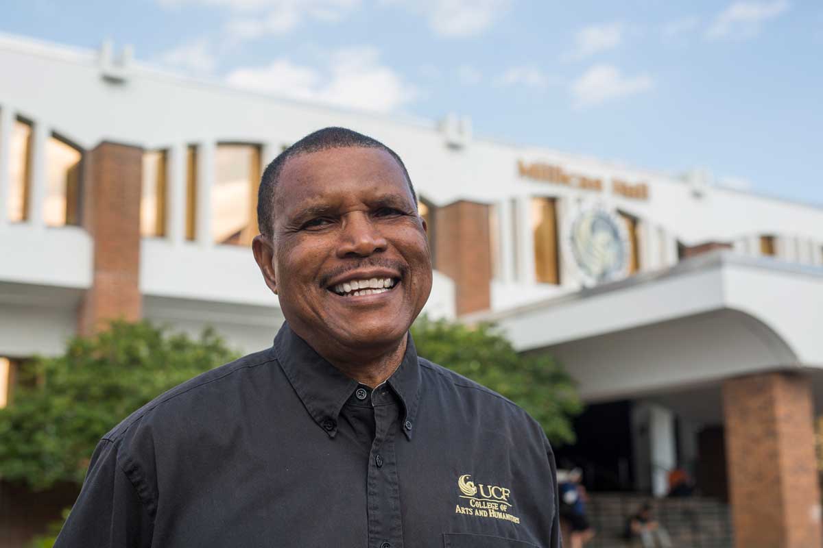 African-American man wearing black long sleeve shirt stands in front of building