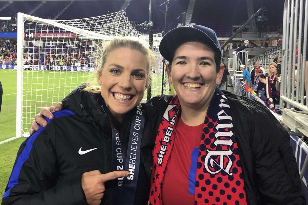 U.S. women's national team player Julie Ertz poses with Ashley Taylor, a fan dressed in red shirt with a red scarf and hat, near soccer field