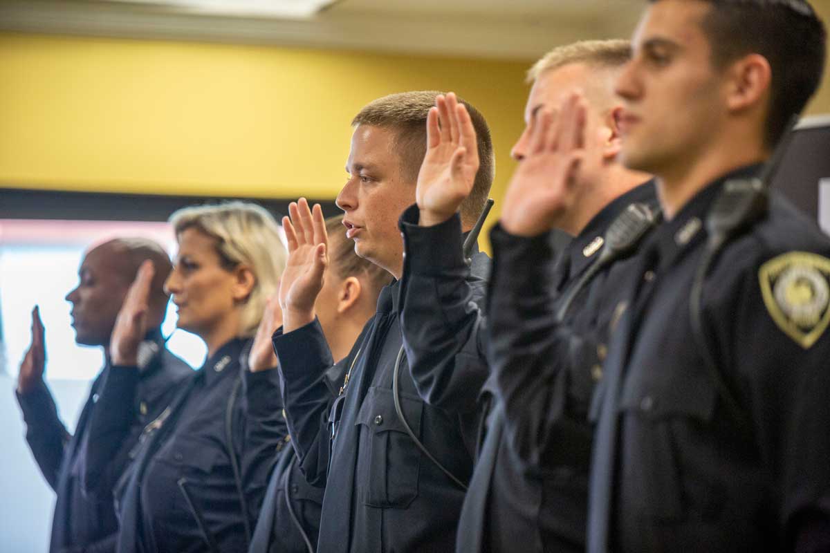 Six officers stand shoulder to shoulder with right hand raised to take oath