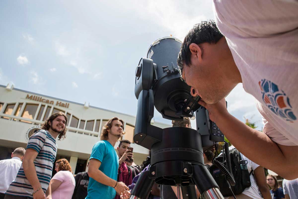 Student looks into telescope in front of Millican Hall