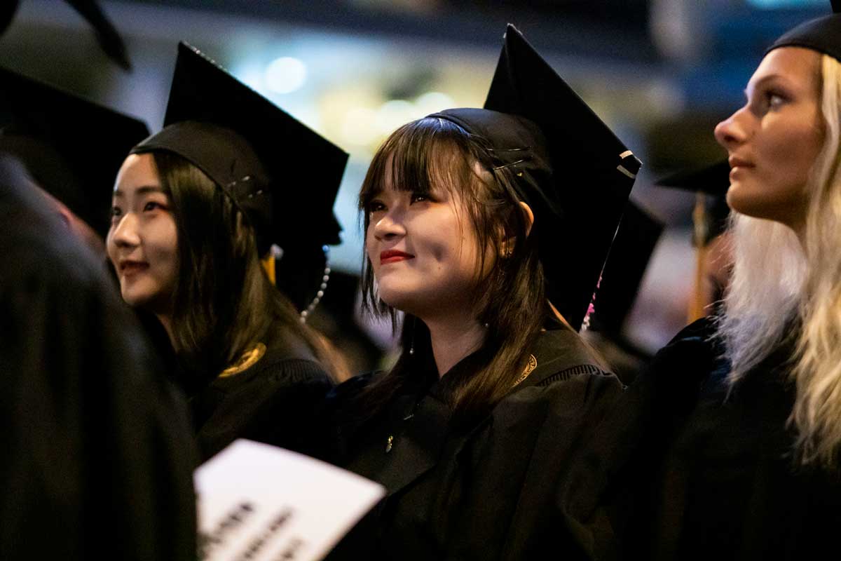 Three females in cap and gowns stand at graduation ceremony