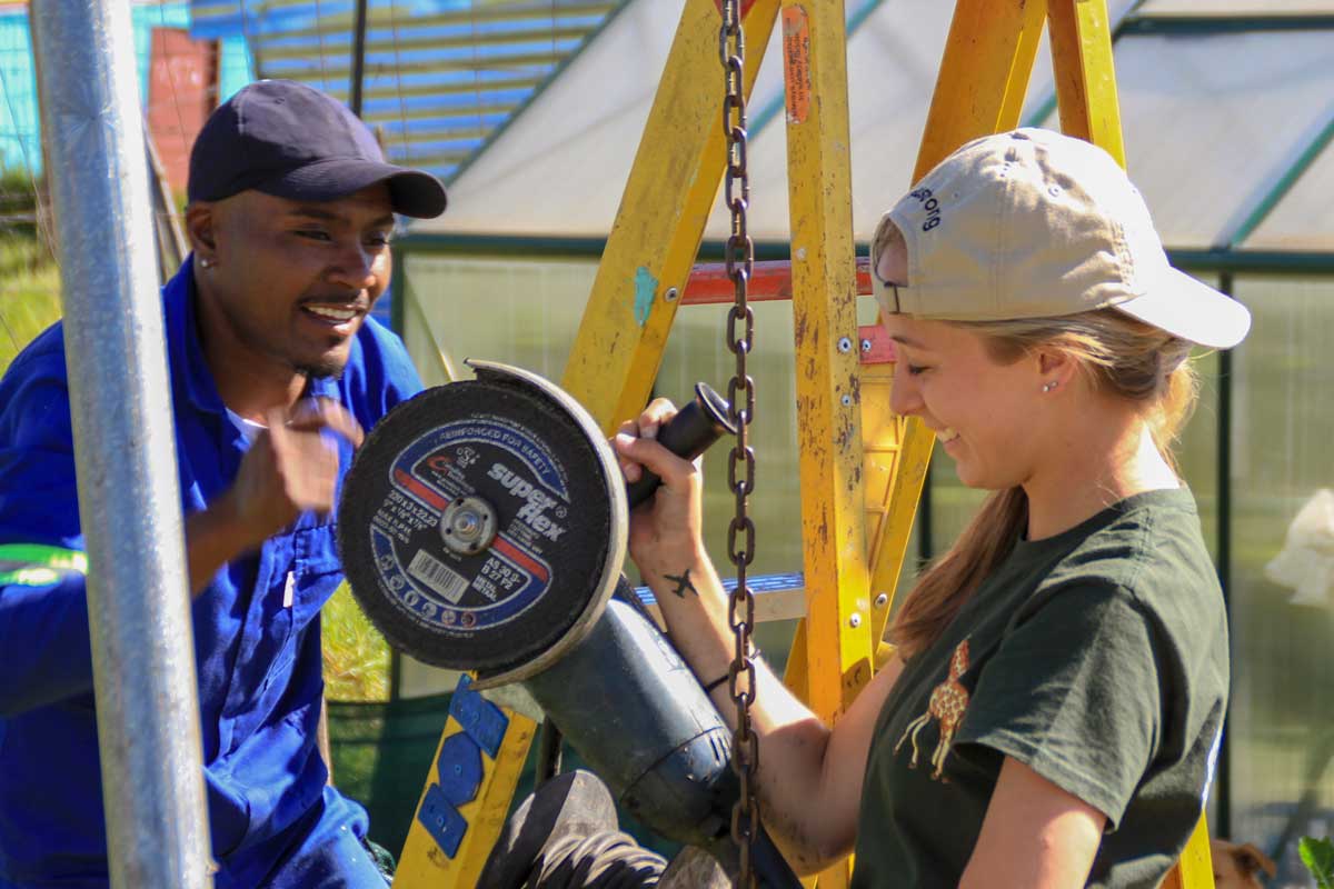 UCF student and man stand next to yellow ladder with a power tool