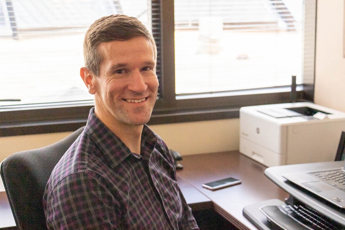 Man in collared shirt sits at a desk with a computer