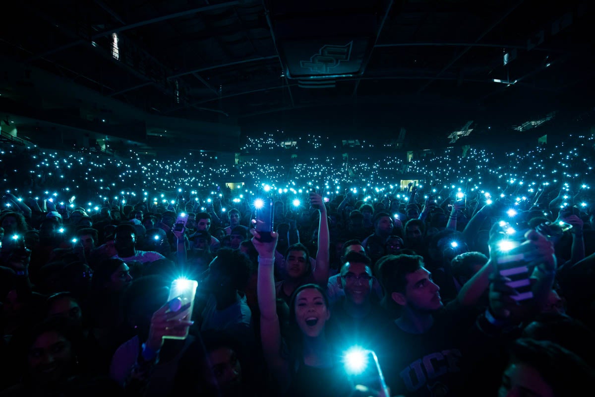 Dark arena with crowd holding up cell phone flashlights