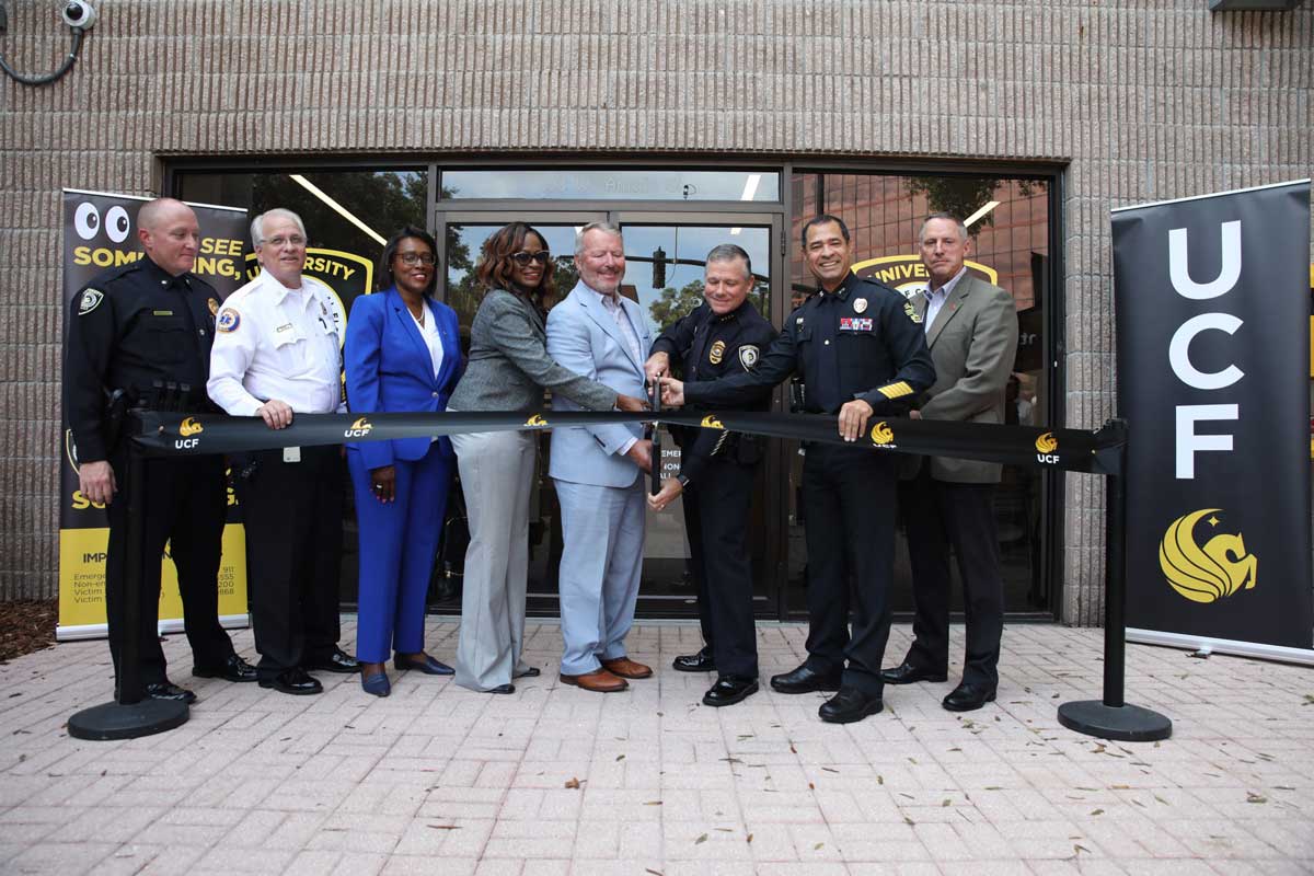 Eight people stand shoulder to shoulder to help cut a ribbon in front of UCF Police's new station at downtown