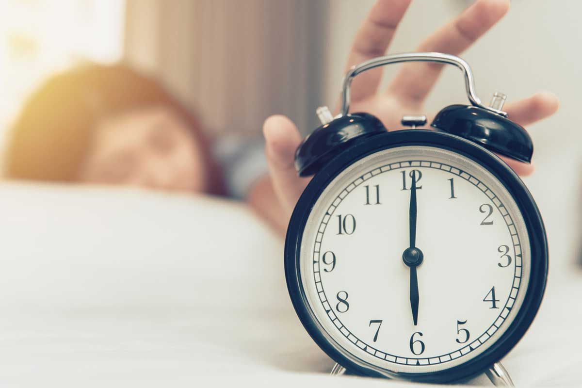 Woman reaches for alarm clock reading 6 a.m.