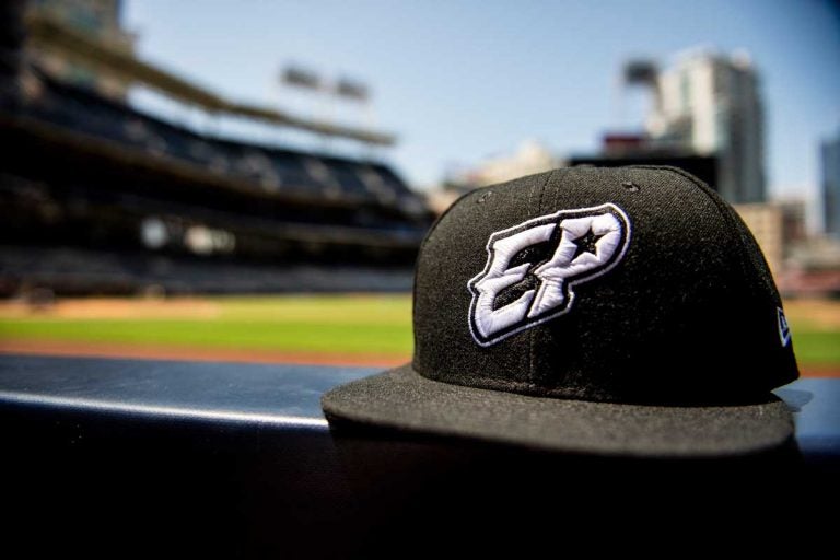 Black baseball hat perched on dugout ledge with baseball field blurred in background