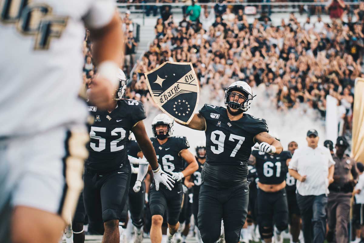 Football team runs out of tunnel onto the field as #97 holds up ChargeOn shield