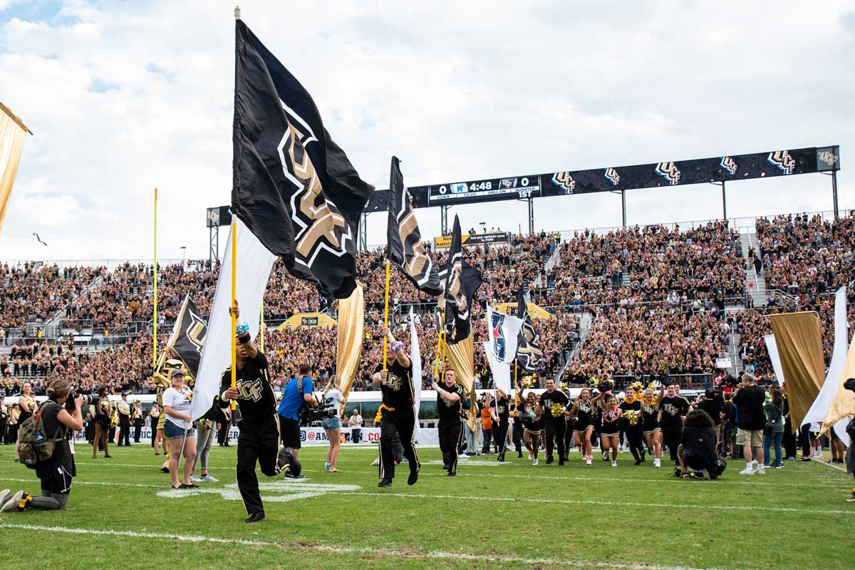 Cheerleaders holding UCF flags storm out onto football field