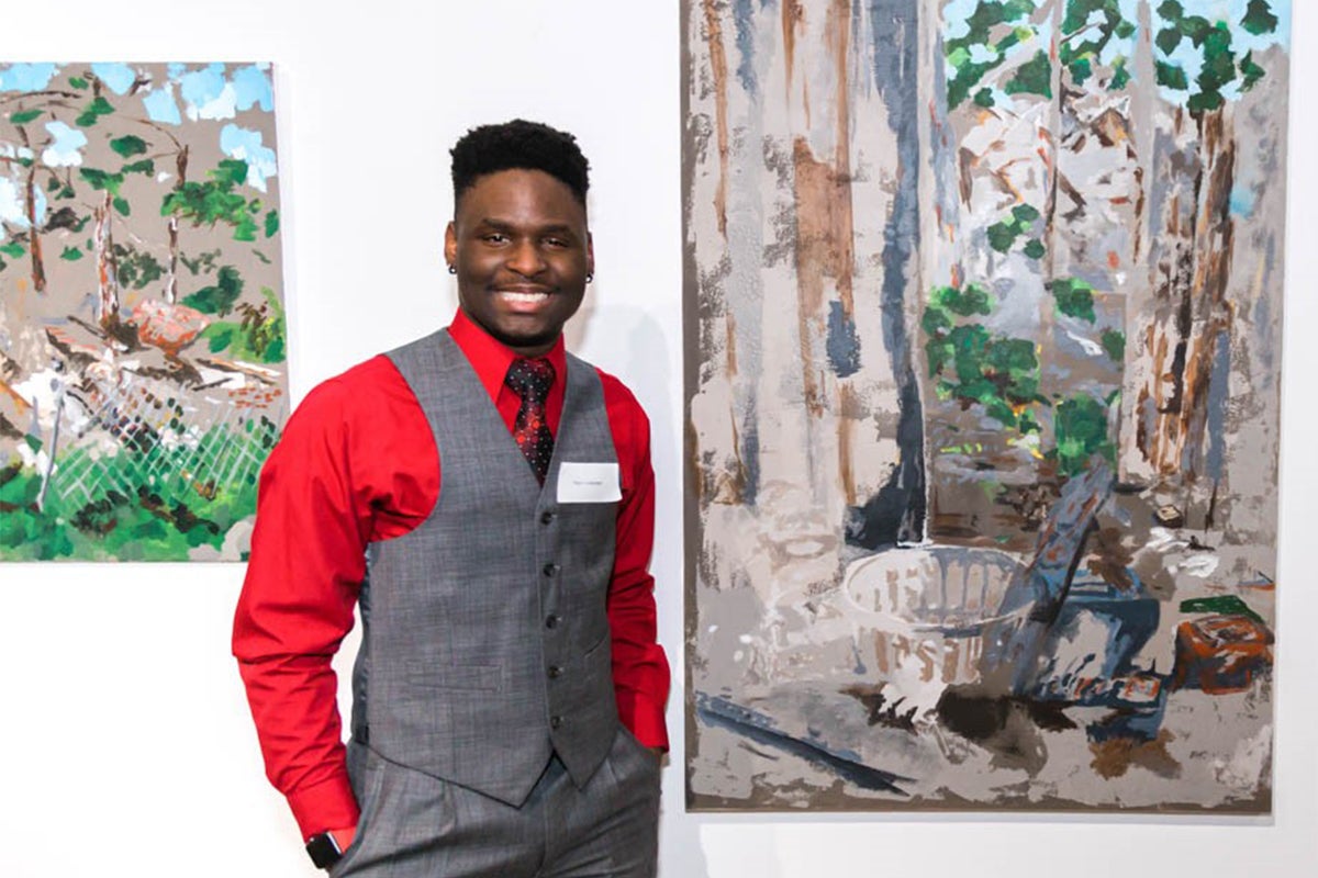 Titus Thomas next to a painting that shows the type of rundown house he used to live in as a young boy.