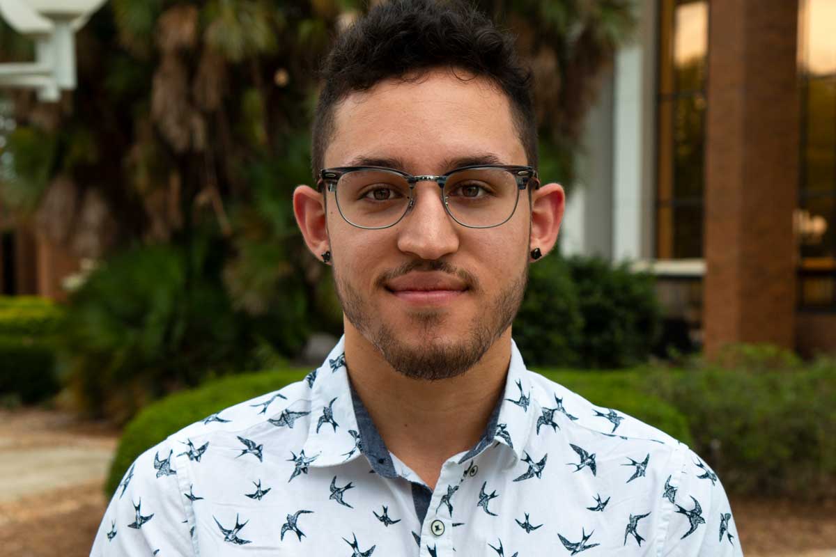 College-age male student wearing glasses and blue patterned collared shirt