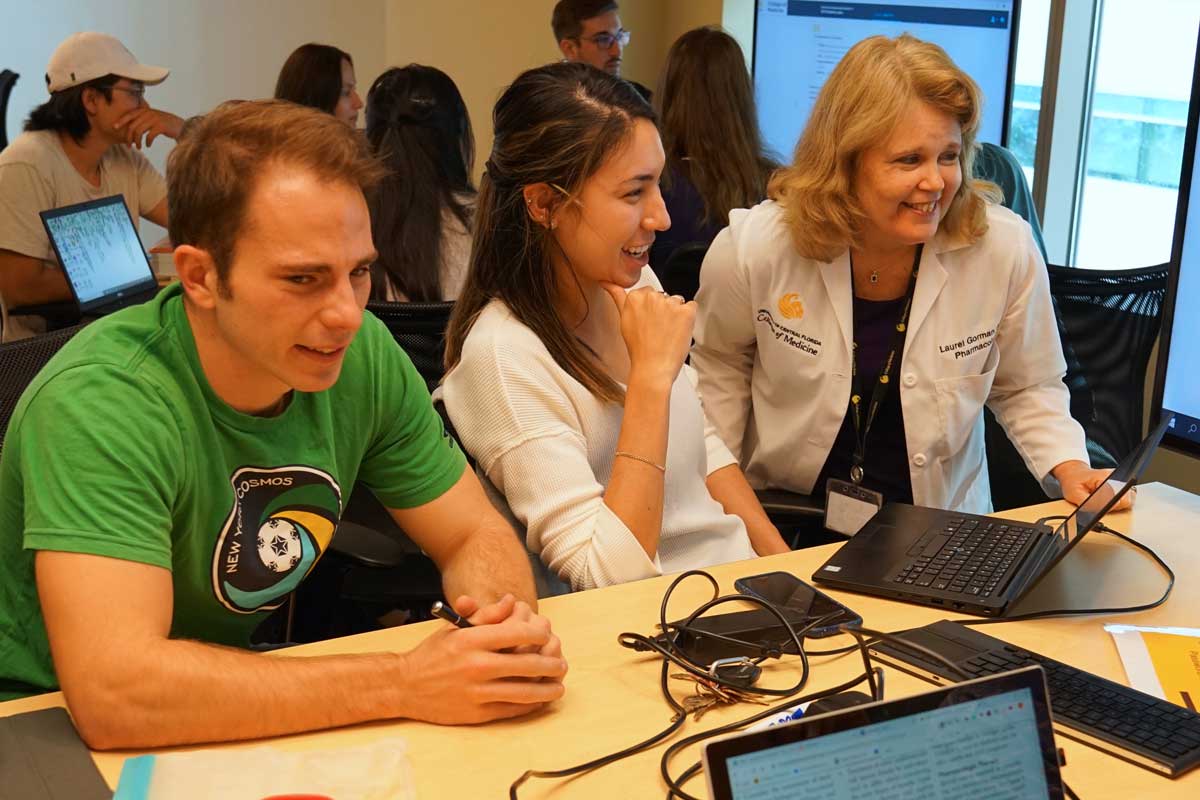 A woman in a medical coat instructs a student seated at a computer