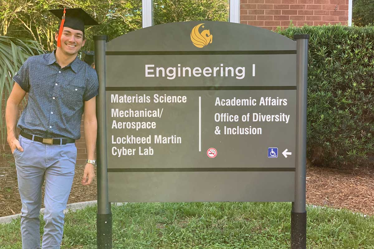 Juan Vila wears graduation cap while standing next to Engineering College sign