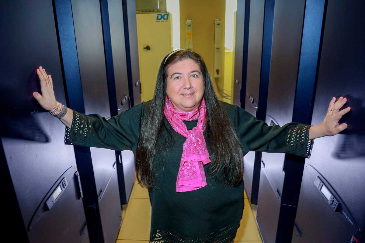 Woman wearing black long sleeve top and pink scarf stands in hallway with arms outstretched