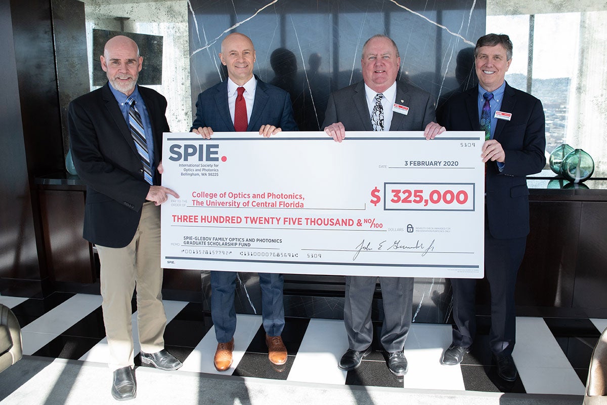 Four men in suits hold up a giant check in the amount of $325,000.
