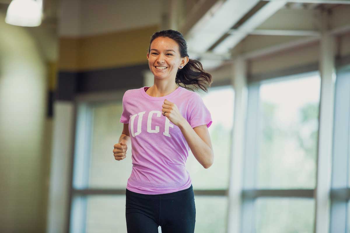 female wearing pink UCF shirt jogs inside