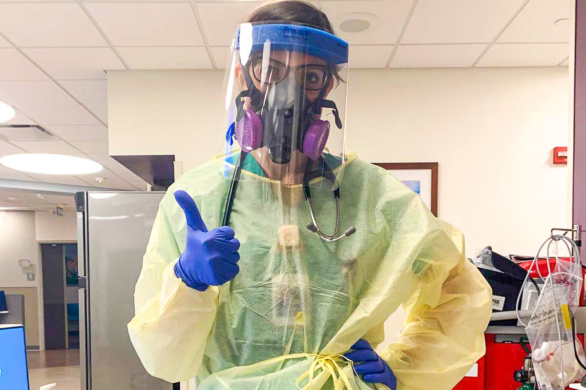 Woman doctor wears yellow scrubs, blue gloves, and face mask