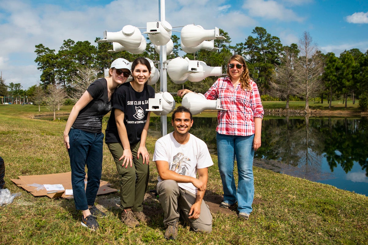 Four students stand in front of a pole with bird houses attached.