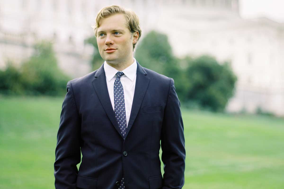 blonde man wearing business suit and tie stands in front of US Capitol Building