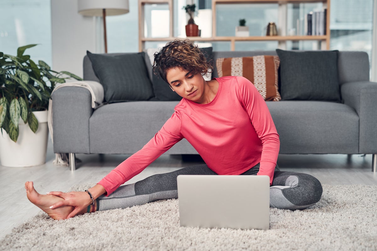 Full length shot of an attractive young woman multitasking and using a laptop while stretching in her living room