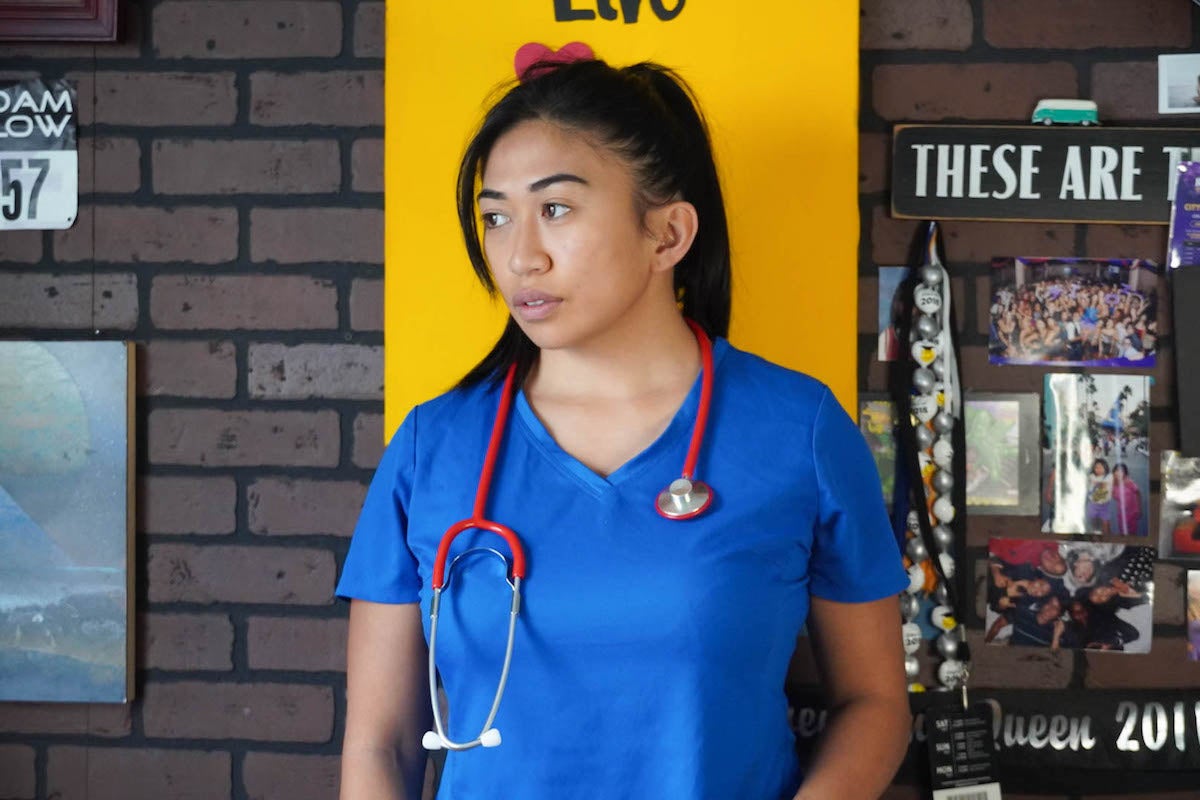 A nurse wears blue scrubs and a red stethoscope.