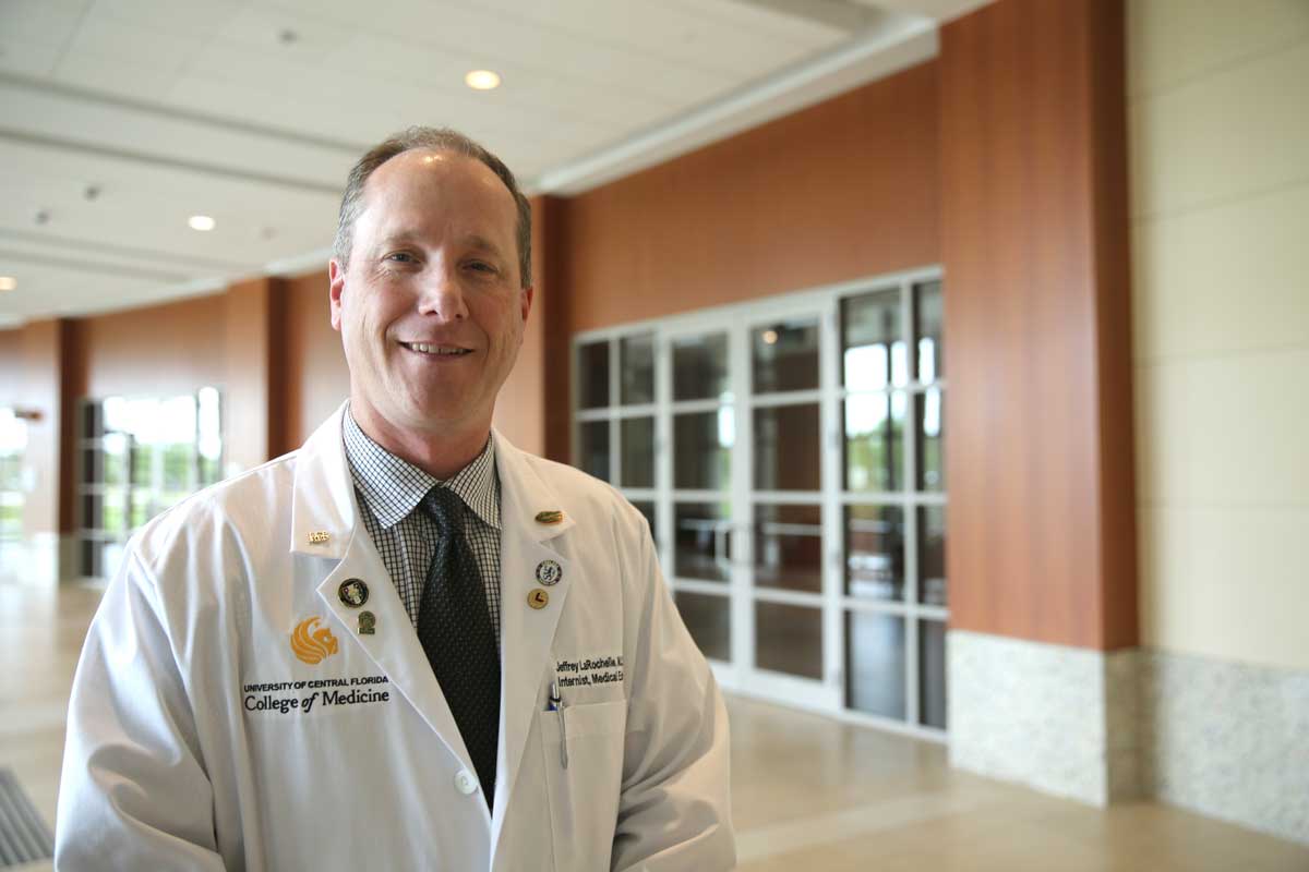 Man wearing College of Medicine white coat stands in front of glass windows