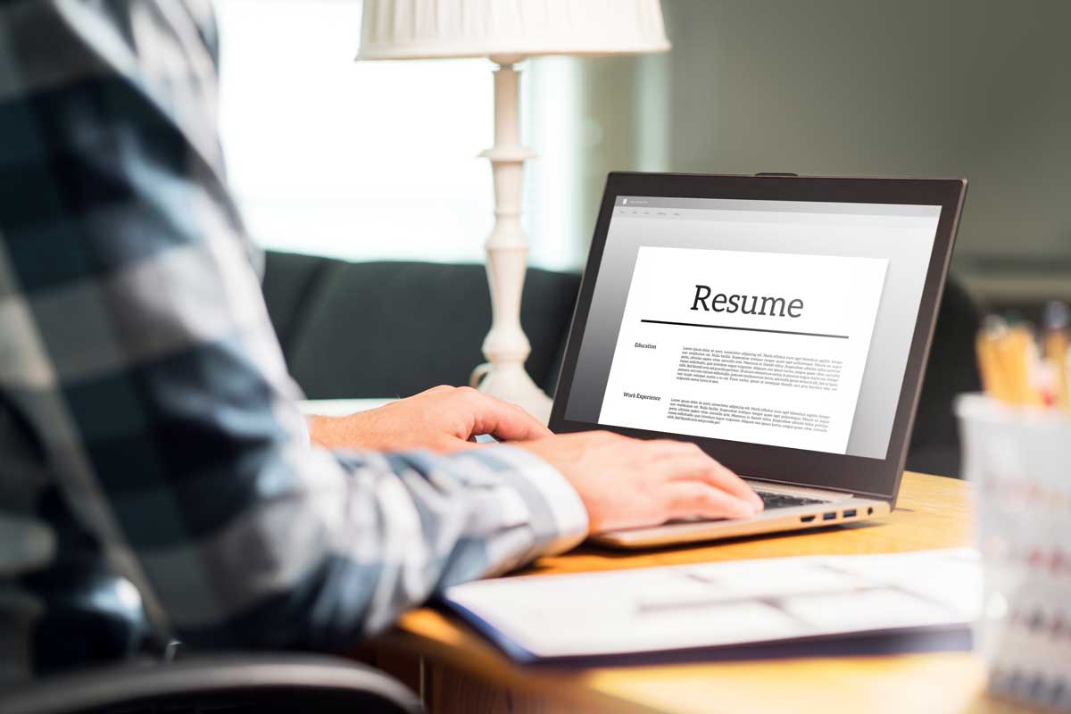 person sits at desk in front of laptop with resume