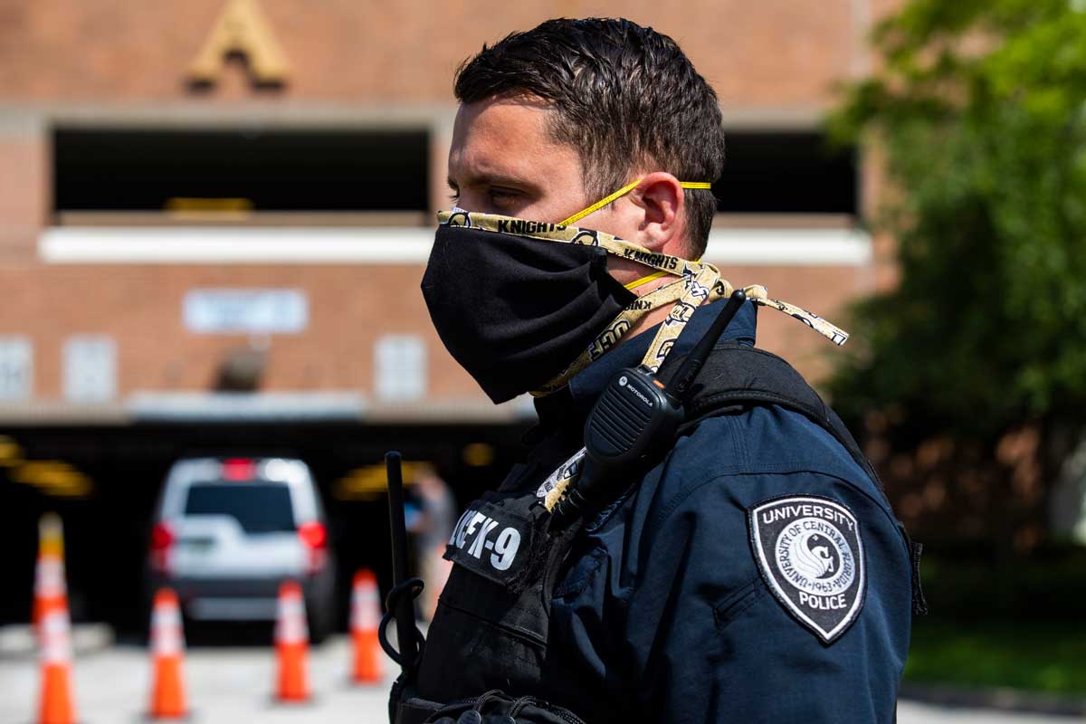 UCF Police officer wears black face mask with UCF theme tie strings, standing outside Garage A