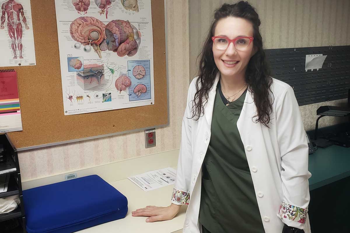 Kellie Chapman, wearing a white nursing coat, stands next to bulletin board with health posters