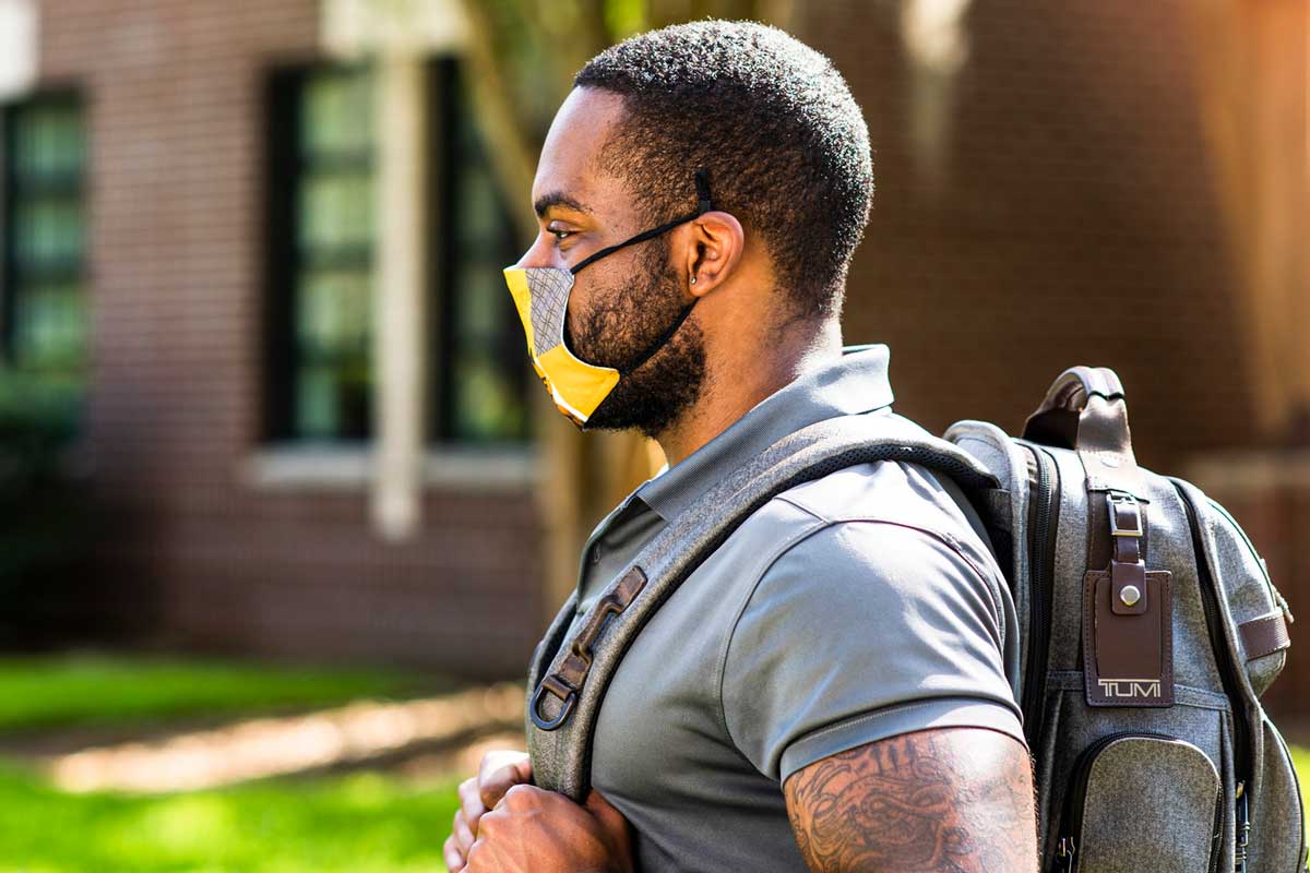 Man wearing backpack and face mask walks on UCF campus