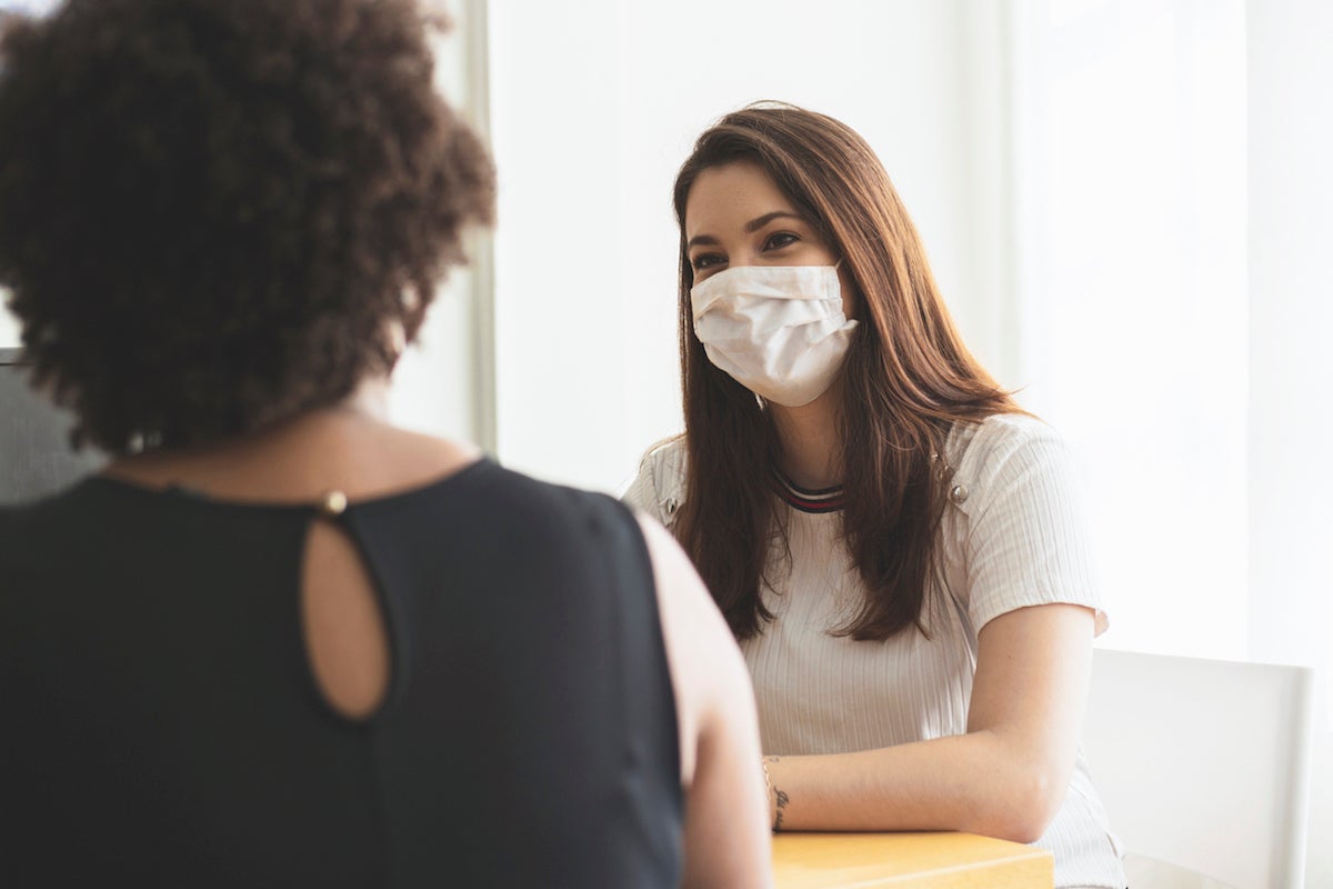 Photo of two young women talking in an office wearing a protective face mask.